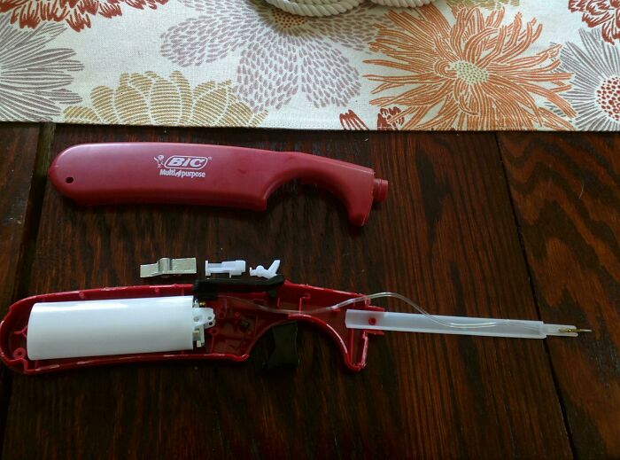 Disassembled Bic multipurpose lighter showing the insides of this common household object on a wooden table.