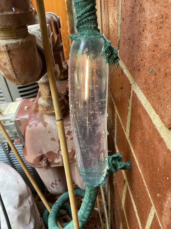 Transparent water-filled section on an old pipe revealing the insides of the object against a brick wall background