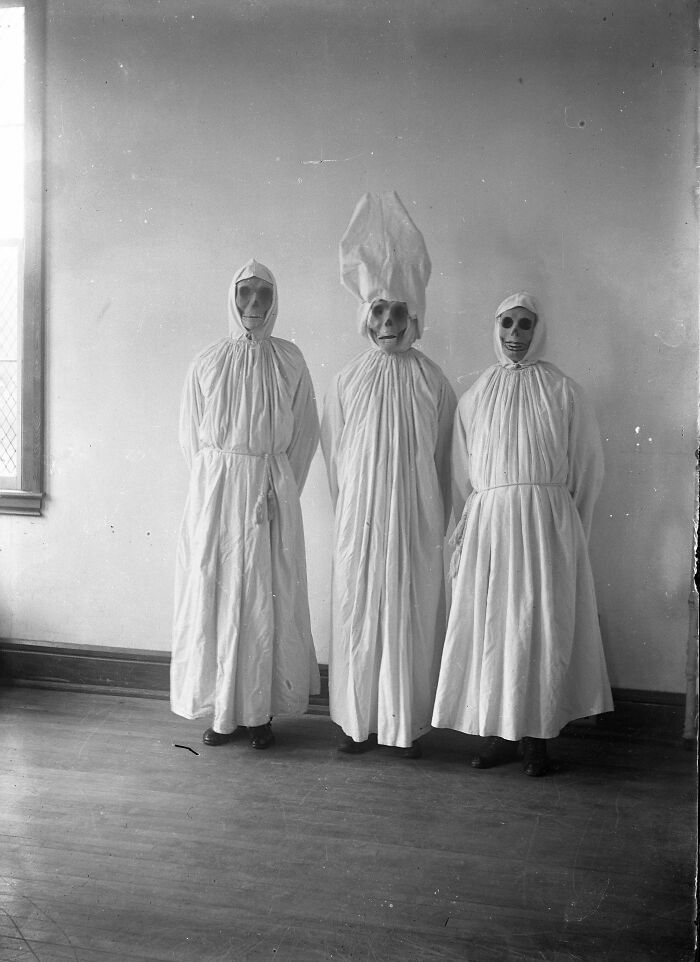 Three people wearing eerie white robes and masks in an utterly unique historical photo with a deep backstory.