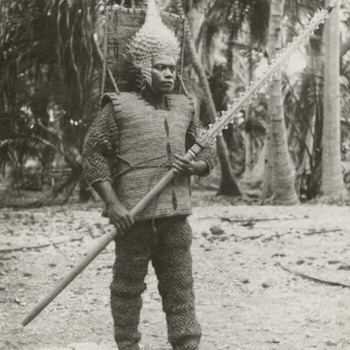 Man in unique traditional armor holding a spiked weapon, captured in a historical photo with a deep backstory.
