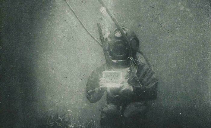 Vintage underwater diver holding a sign underwater captured in an utterly unique historical photo with a deep backstory