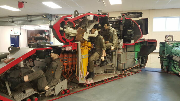 Cutaway view of a military vehicle interior showing detailed mechanics and mannequins operating controls inside.