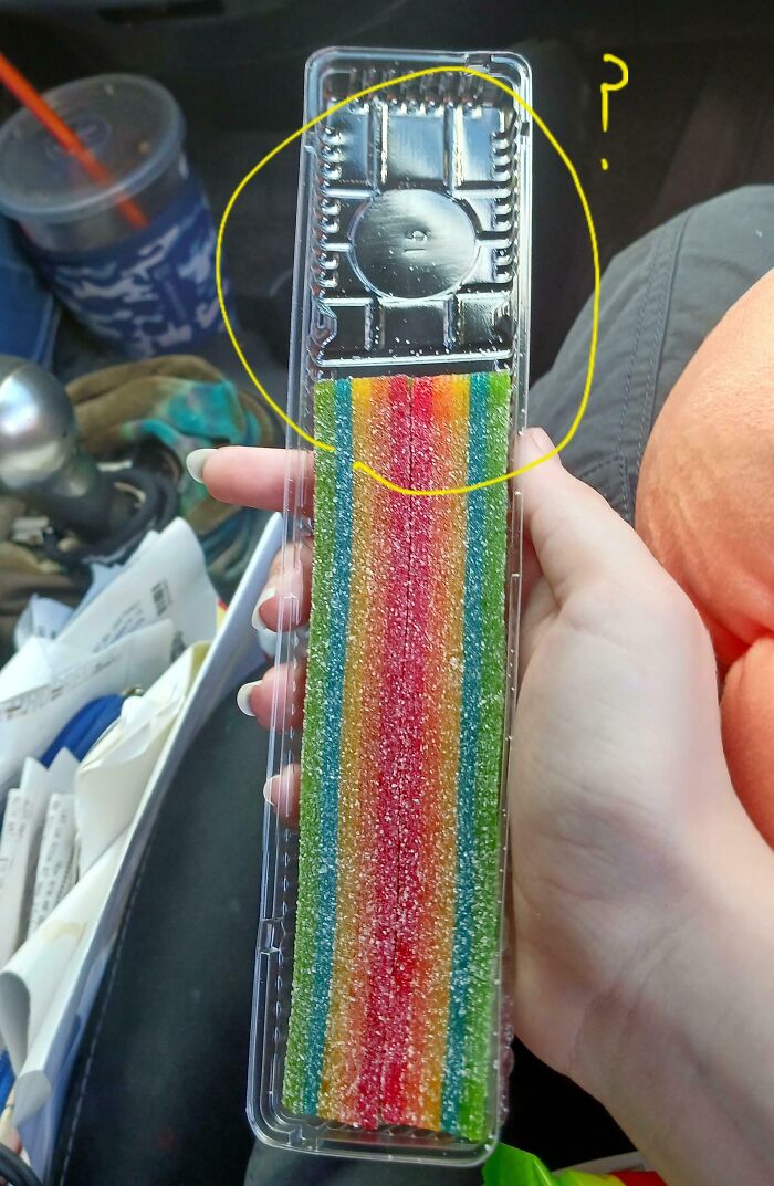 Hand holding a misleading packaging with a small candy strip and large empty plastic tray, example of product packaging.