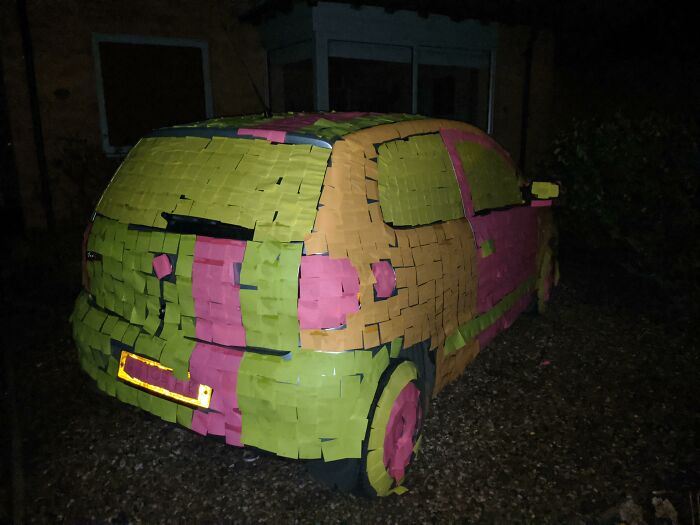 Car covered in colorful sticky notes at night, illustrating a petty revenge prank on a parked vehicle.