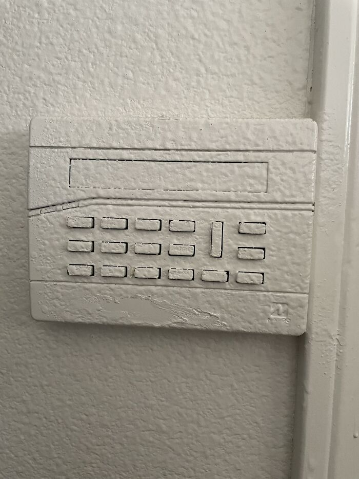 Security keypad painted over entirely in white on a textured wall as a funny example of people not even trying.