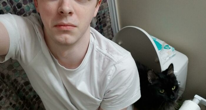 Young man in a white shirt sharing personal space with a black cat in a bathroom, illustrating pets and personal space challenges.