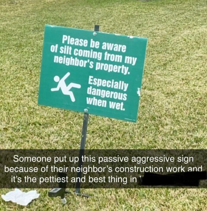 Green sign warns about slippery silt from neighbor's property, showing an example of petty revenge and passive aggression.