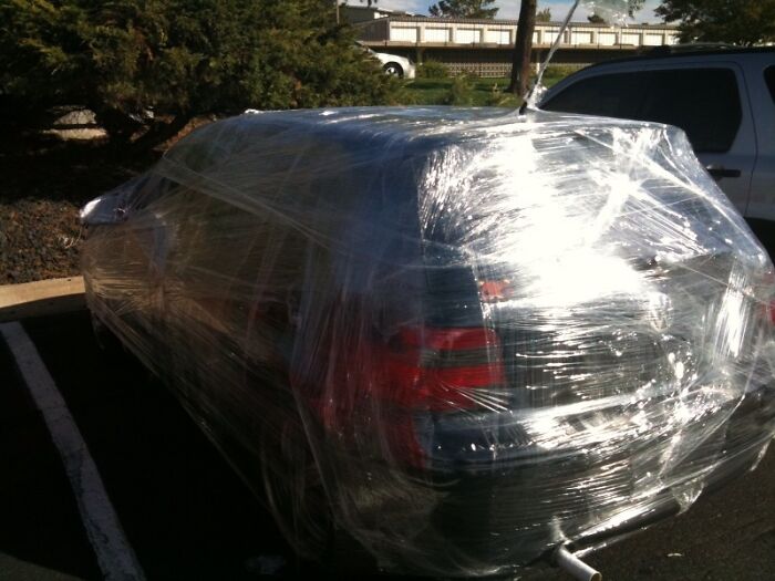 Car wrapped entirely in clear plastic wrap in a parking lot as an example of petty revenge prank.