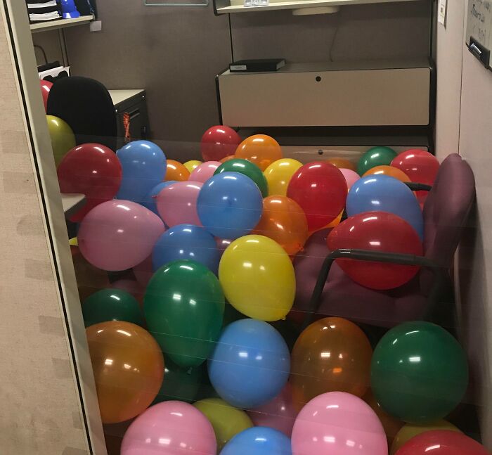 Office cubicle filled with colorful balloons as a petty revenge prank in a workplace setting.