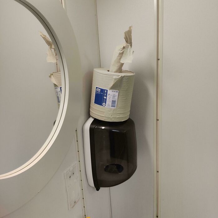 Roll of paper towels placed on top of a soap dispenser inside a bathroom, showcasing people not even trying.