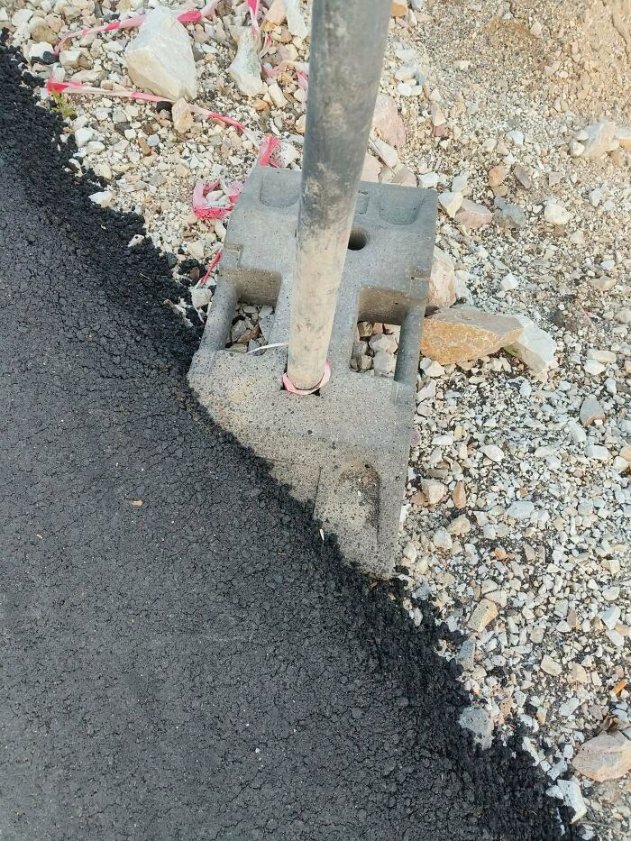 Concrete block placed over fresh asphalt with pole, illustrating funny examples of people not trying in work.