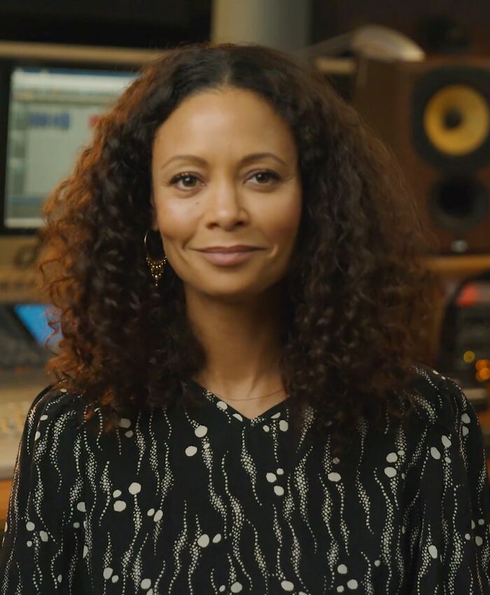 Thandiwe Newton with curly hair and patterned top, sitting in a recording studio highlighting her bio and career.