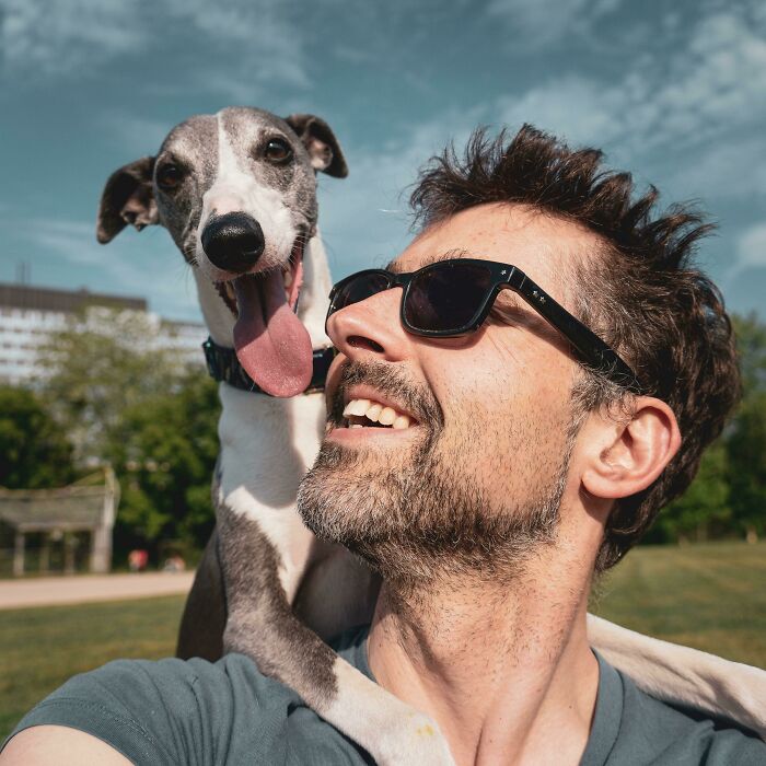 Man wearing sunglasses takes a selfie with a happy dog on his shoulder, showcasing animals who can take better selfies.