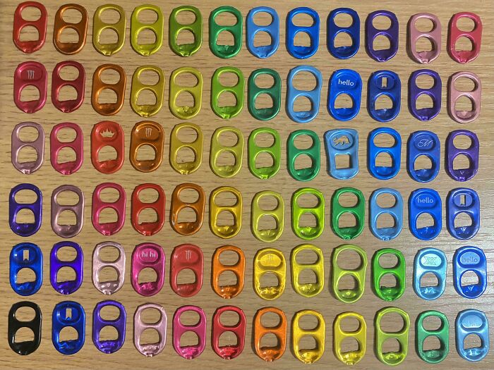 Coloful soda can tabs arranged neatly in rows on a wooden surface, showcasing satisfying order and organization.