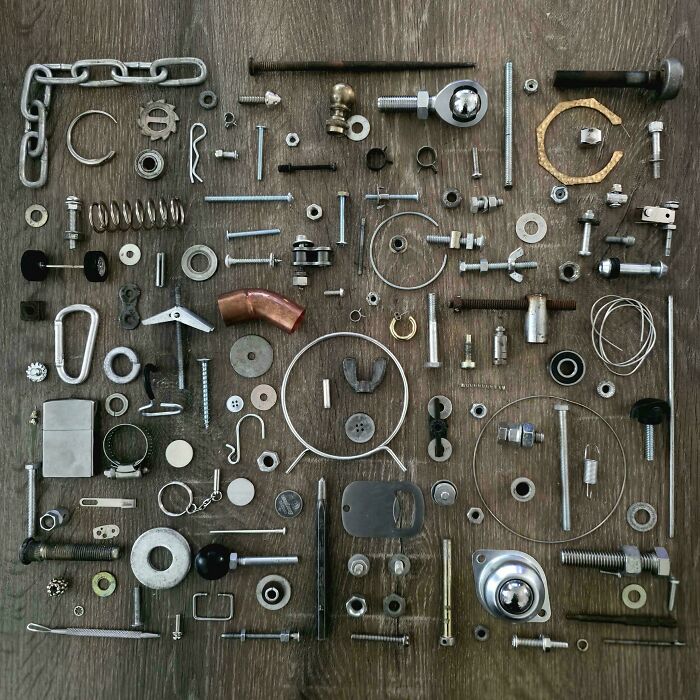Various small metal parts neatly arranged in a grid on a wooden surface, showcasing all things knolled organization.