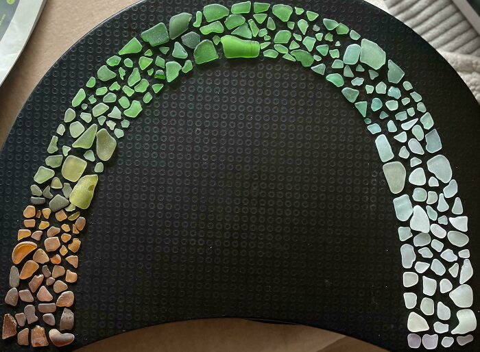 Colorful sea glass pieces neatly arranged by size and color gradient on a black surface, showcasing perfect knolled order.