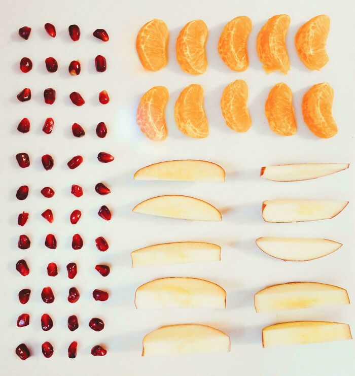 Neatly arranged rows of pomegranate seeds, orange slices, and apple wedges showcasing order and balance.