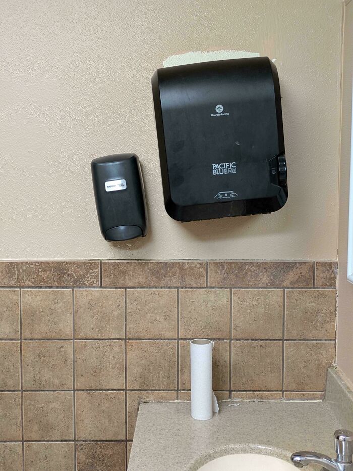 Paper towel dispenser mounted too high with empty paper towel roll below, a funny example of people not even trying at work.