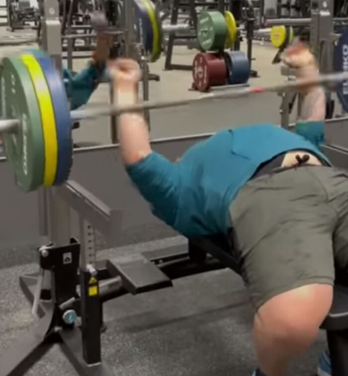 Man performing bench press in gym, captured in a frozen frame showcasing strength and weightlifting technique.
