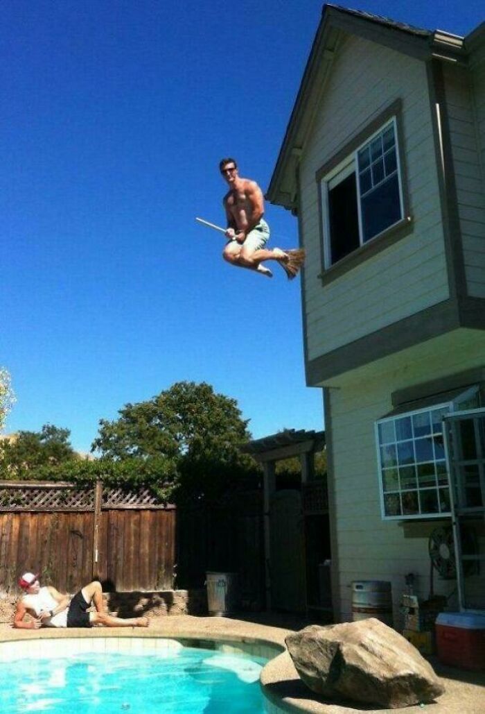 Shirtless man captured in a frozen frame mid-air above a pool, holding a broomstick as if flying from a house window.