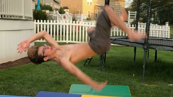 Teen boy mid-air doing a backflip in a backyard trampoline scene, captured as a frozen frame action shot.