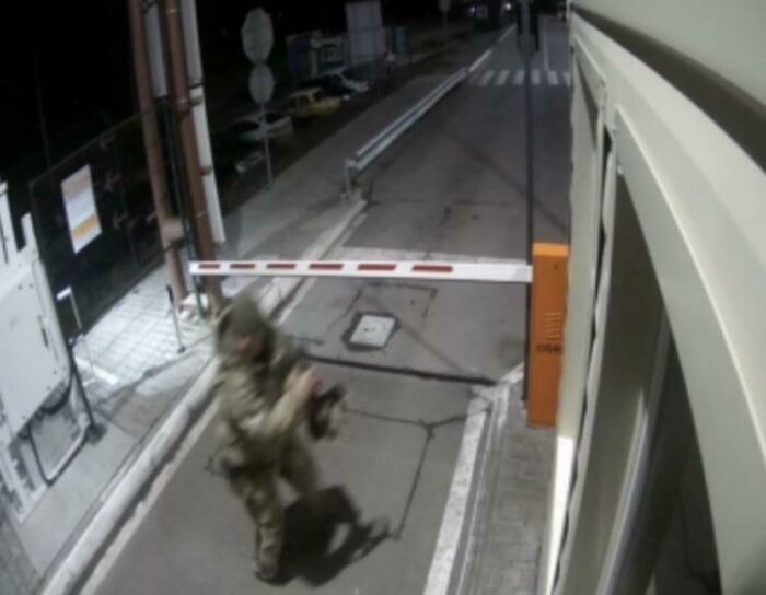 Person in camouflage clothing caught in a frozen frame near a security gate barrier at night on a street.