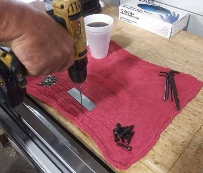 Hand using drill on metal piece with screws, wrenches, and gloves on workbench in 84 frozen frames series.