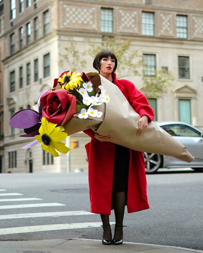 Woman in a red coat holding an oversized bouquet of creative paper flowers on a city street, showcasing cool projects.
