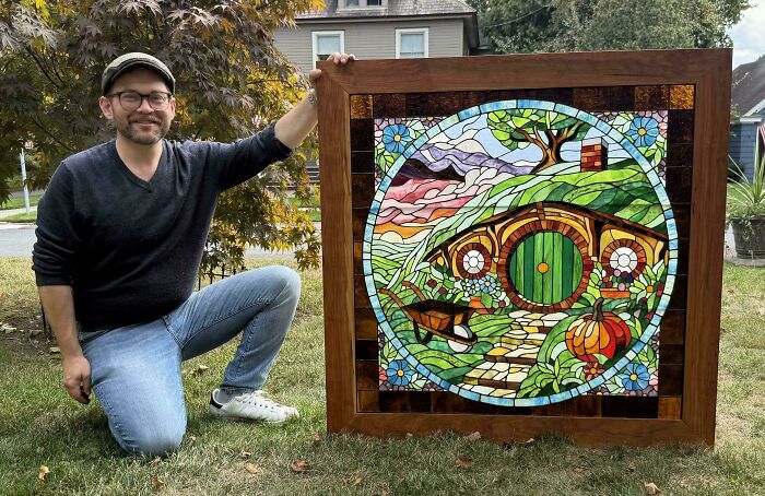 Man showcasing a creative stained glass artwork of a colorful hobbit house outdoors, highlighting creative projects.