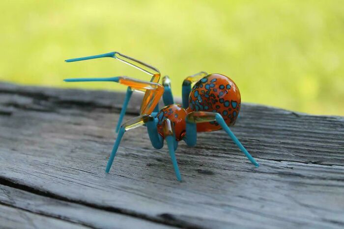 Colorful creative spider sculpture made from glass and metal displayed on wooden surface outdoors.