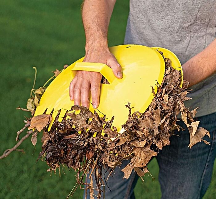 Person using yellow garden leaf collector to gather dry leaves, essential garden prep before the first freeze.