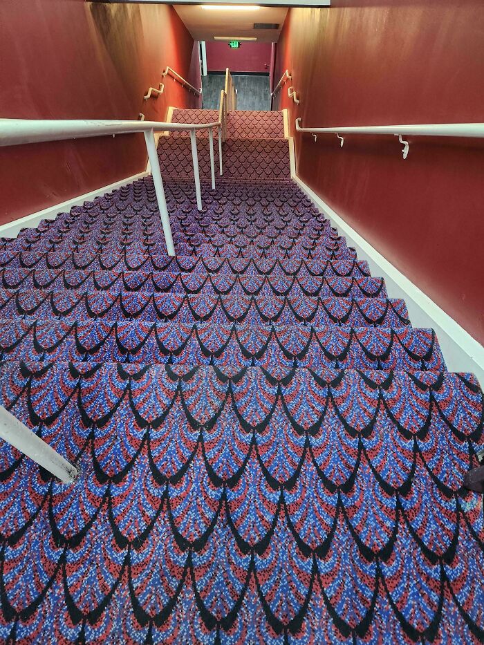 Steep carpeted stairs with red walls and multiple handrails in an Airbnb setting showing a unique patterned design.