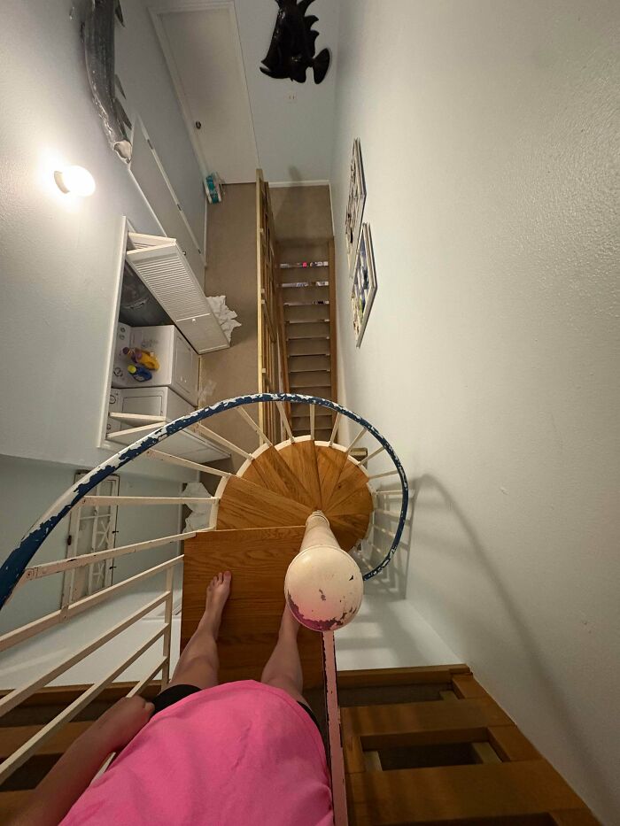 View looking down a narrow spiral staircase with wooden steps and a person in a pink shirt at the top in an Airbnb setting.