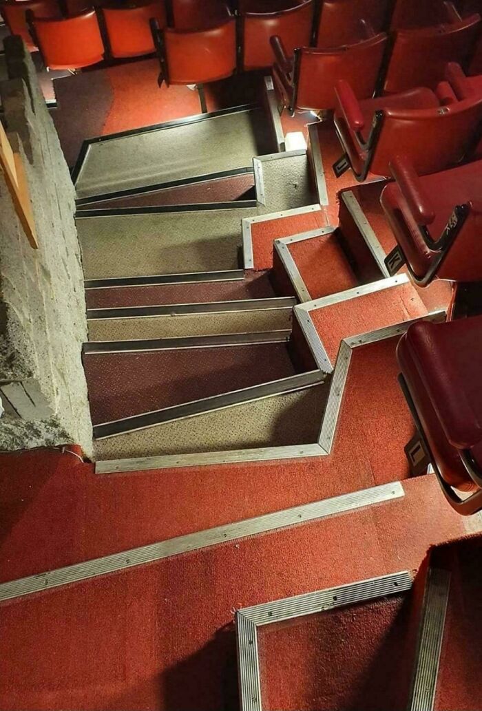 Steep, narrow, and zigzagging stairs in a theater with red seats, illustrating Airbnb insanity staircase hazards.