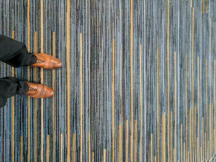 Person wearing brown dress shoes standing on a striped carpet, relating to Airbnb insurance and stair safety concerns.