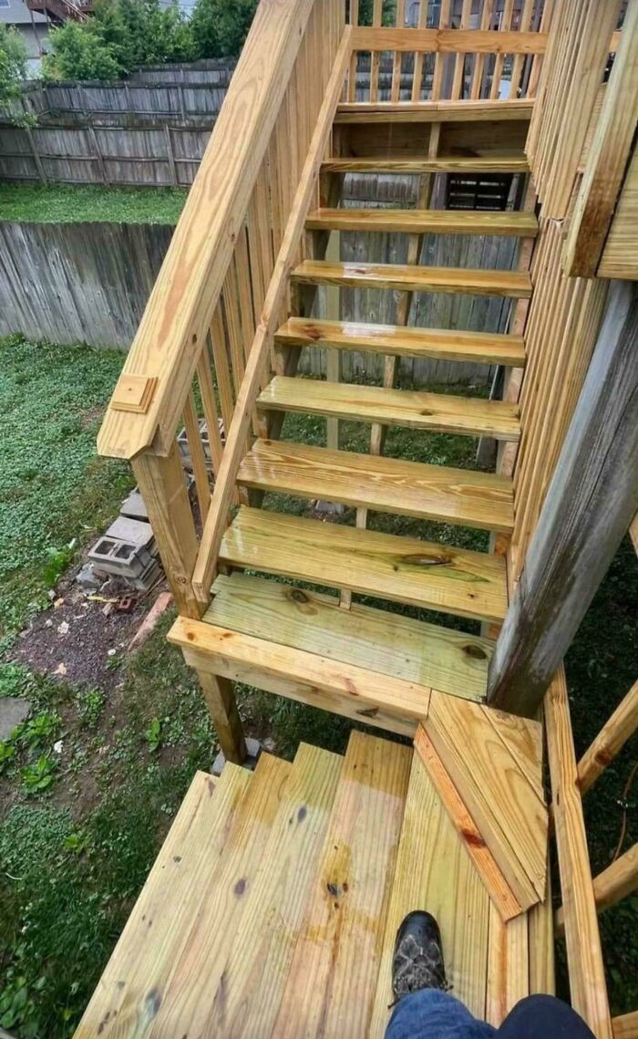 Wooden Airbnb stairs with irregular gaps and multiple flights, viewed from the top step outdoors near a fenced yard.