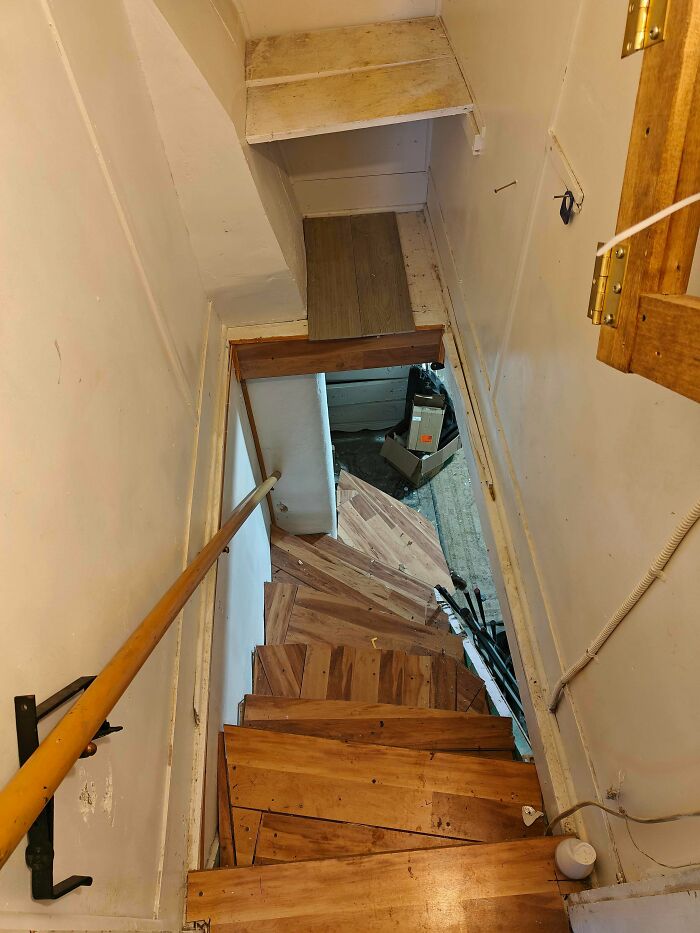 Steep narrow wooden stairs with irregular steps and a handrail in a cramped indoor space needing Airbnb insurance.