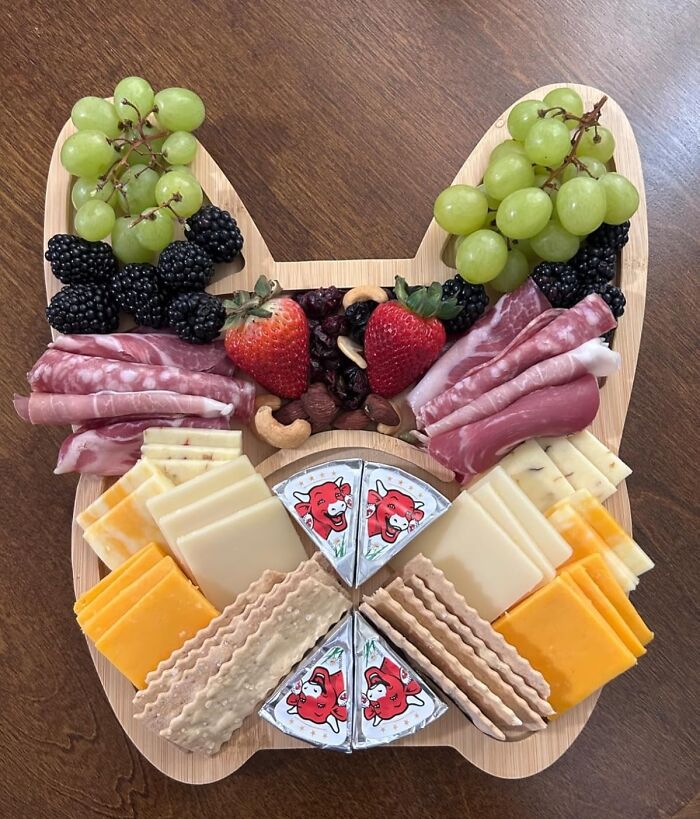 Cat-shaped wooden novelty cheese board with assorted cheese, meats, fruits, and crackers arranged neatly.