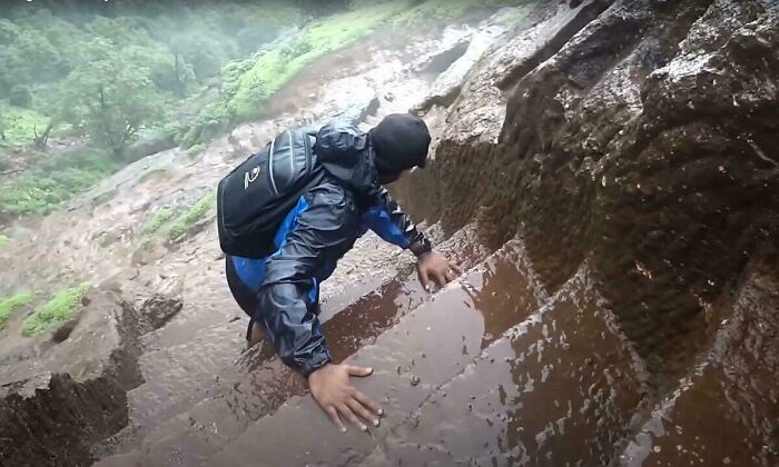 Person in a rain jacket climbing slippery, narrow stone stairs outdoors, illustrating Airbnb insanity and safety risks.