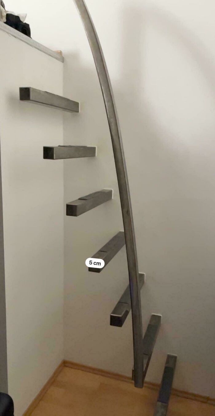 Minimalist metal stairs attached to a wall with a curved handrail, illustrating Airbnb insanity with a risky design.