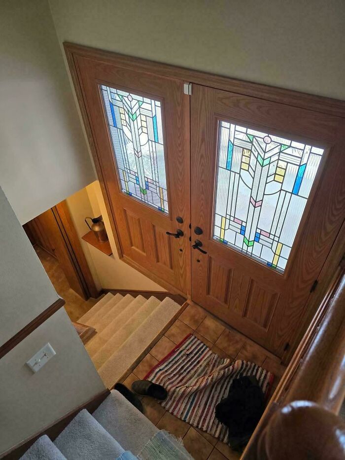 Steep indoor stairs leading to a wooden door with stained glass panels, highlighting Airbnb insurance safety concerns.