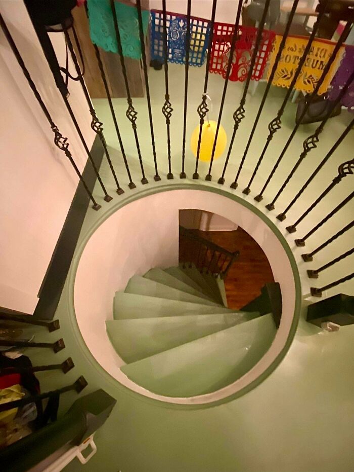 Spiral staircase with green steps and black iron railing inside a colorful Airbnb rental property.