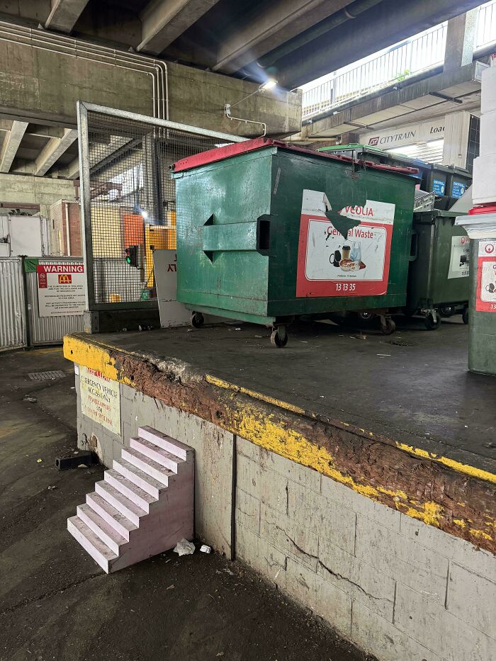 Small model staircase leading up to a loading dock with large green trash bins, illustrating Airbnb insanity stairs concept.