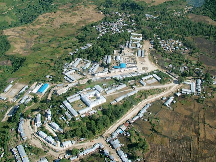 Aerial view of a remote village with scattered buildings surrounded by green fields and hills, showcasing remote locations.