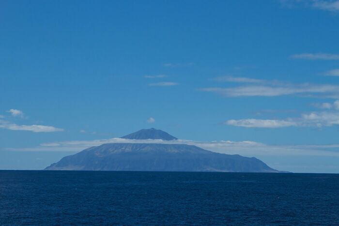 Remote volcanic island rising from deep blue ocean under a clear sky, showcasing mind-blowing remote locations.