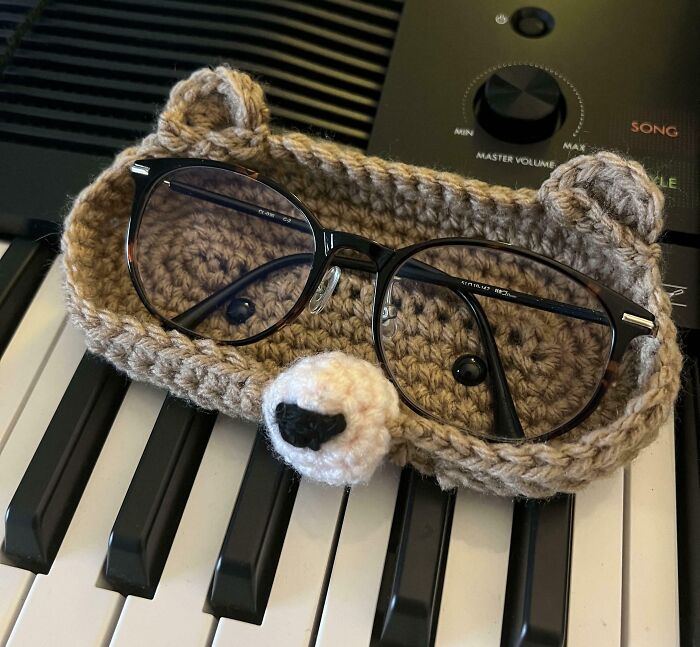 Crocheted bear-shaped glasses holder resting on piano keys, showcasing creative people and cool projects.