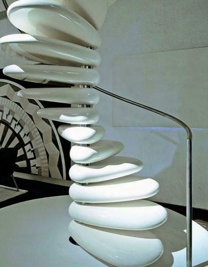 Spiral staircase made of smooth white steps with a metal handrail in a modern interior setting.