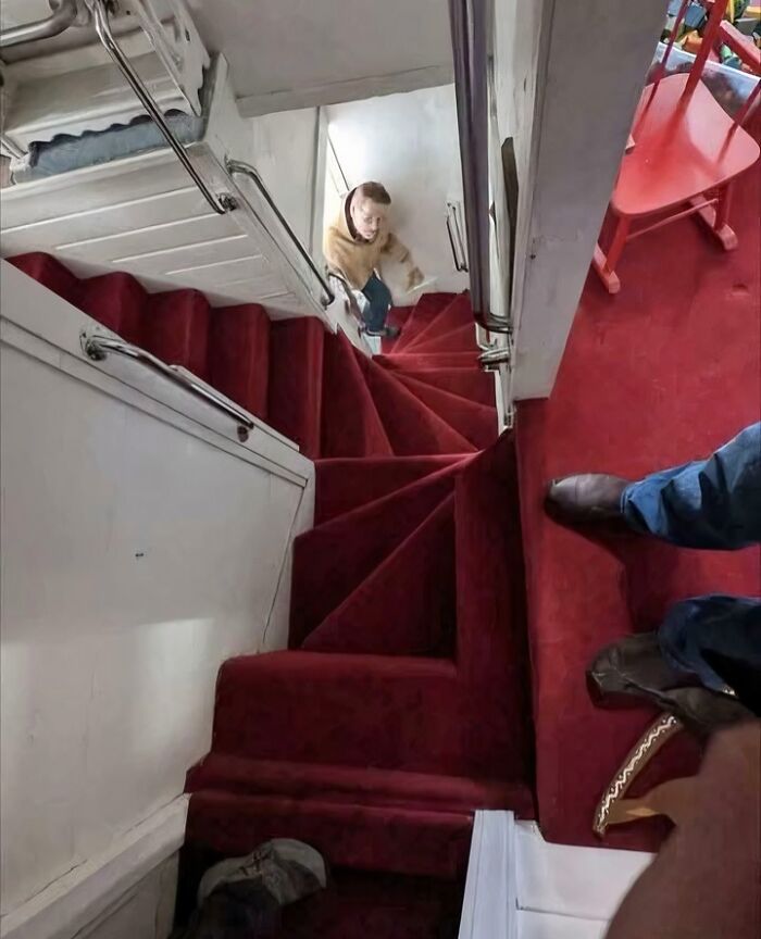 Steep spiral red carpeted stairs in an Airbnb, viewed from above with a person climbing, illustrating Airbnb stairs challenge.