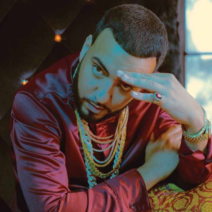 French Montana posing in a red satin shirt with gold chains and rings, reflecting on his bio and career highlights.