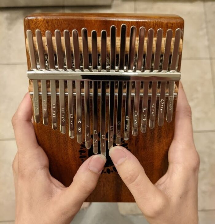 Hands playing a wooden kalimba with metal tines, a unique gift idea for people who are impossible to shop for.